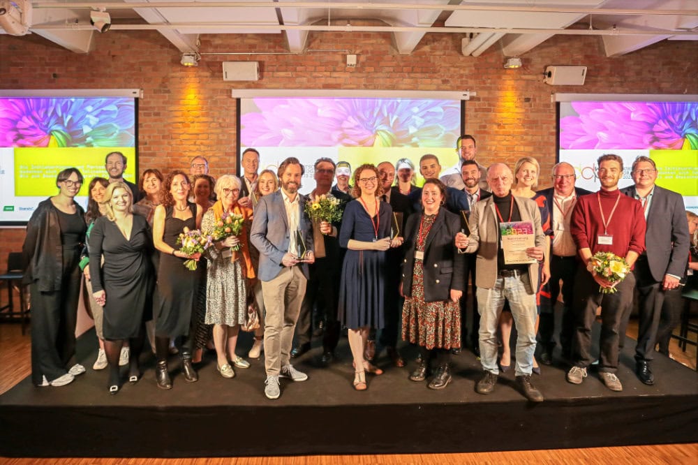 Gruppenfoto eines Firmen-Events auf Bühne mit großer Leinwand – Eventfotografie Unternehmensveranstaltung