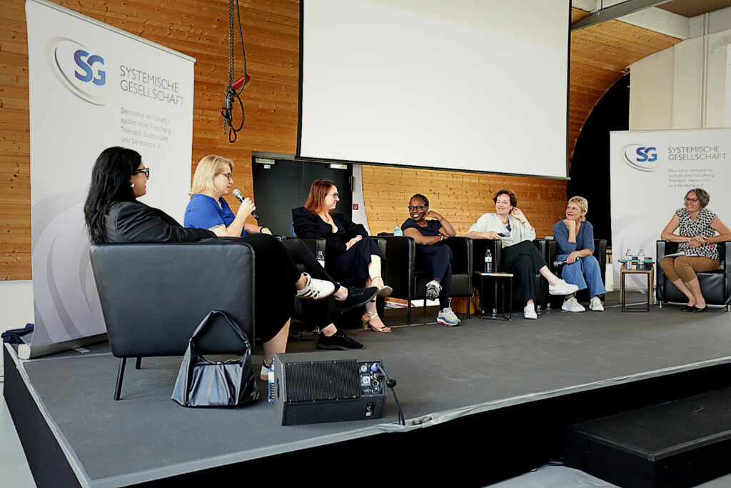 Podiumsdiskussion mit mehreren Sprecherinnen und Sprechern auf Bühne – Eventfotografie Konferenz