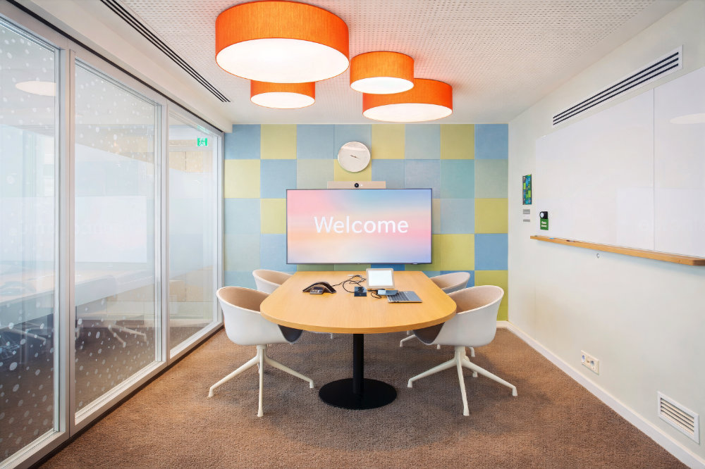 Design-Meetingraum mit runder Tischgruppe, farbiger Wand und Pendelleuchten – Architekturfotografie Büro