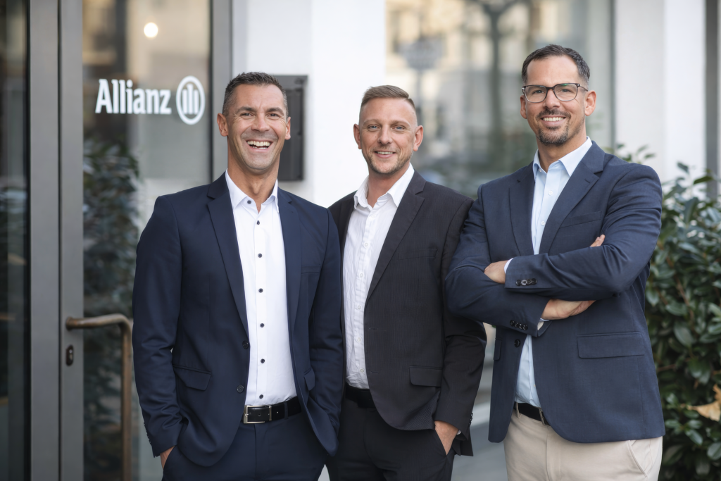 Gruppenfoto von drei Mitarbeitern im Anzug vor Unternehmenslogo – Teamfoto für Firmenwebsite