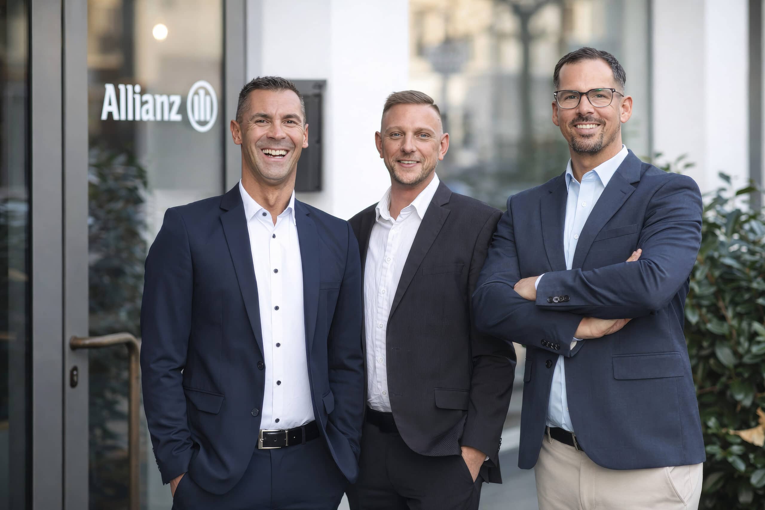 Gruppenfoto von drei Mitarbeitern im Anzug vor Unternehmenslogo – Teamfoto für Firmenwebsite