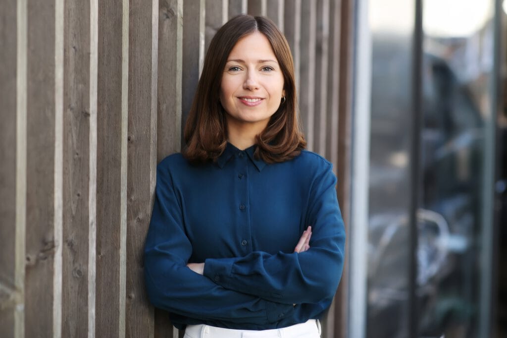 Bewerbungsfoto einer Person in blauer Bluse vor urbaner Holz- und Metallwand – authentisches Portrait für Bewerbung